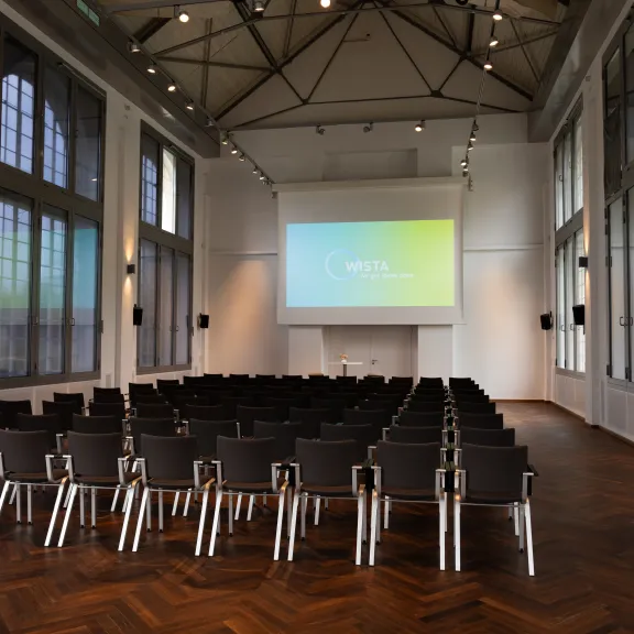 Leerer Konferenzraum mit Stuhlreihen und großer Leinwand vorne.