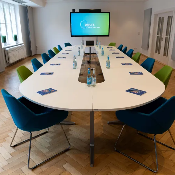 Moderner Konferenzraum mit ovalem Tisch, bunten Stühlen und Präsentationsbildschirm