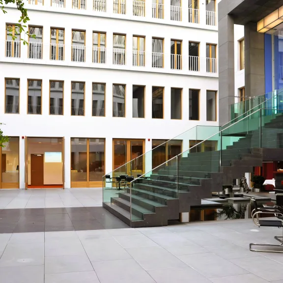 Modernes, helles Atrium mit Glastreppe und Tischen, große Fenster im Hintergrund.