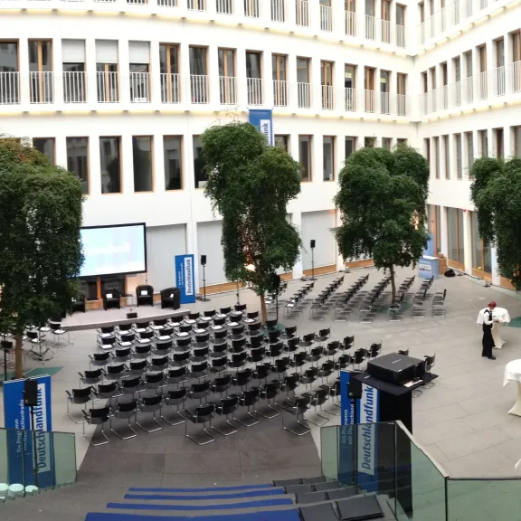 Geordneter Innenhof mit Stuhlreihen, Bäumen und Bühne, bereit für eine Veranstaltung.