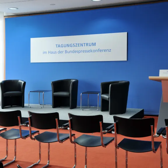 Leerer Konferenzraum mit Bühne, Stühlen und Rednerpult vor blauer Wand