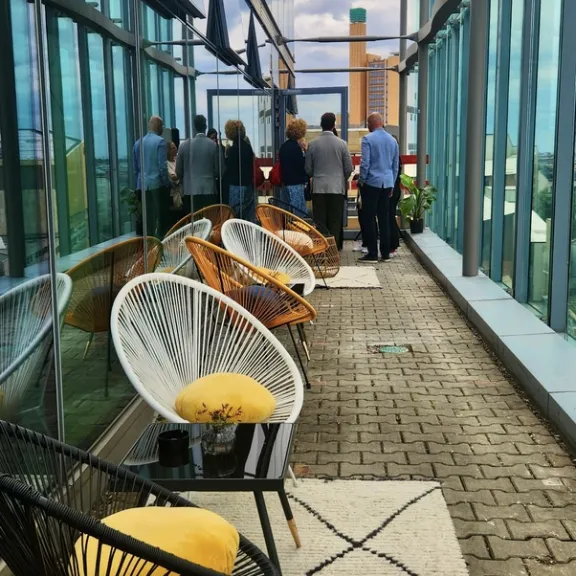 Moderne Terrasse mit Glaswänden, bunten Stühlen und Menschen im Hintergrund