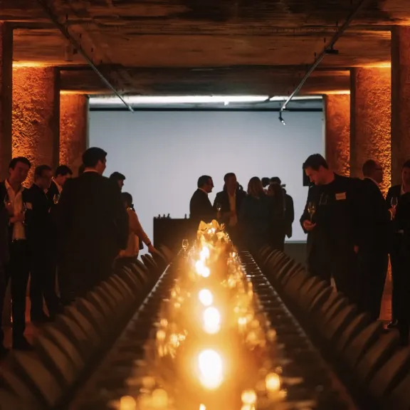 Stimmungsvoll beleuchteter Saal mit gedecktem Tisch und Menschen im Hintergrund.