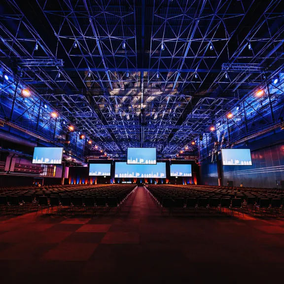 Große Halle, blau beleuchtet mit mehreren beleuchteten Displays, welche von der Decke hängen.