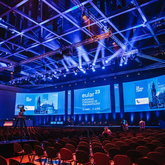 Großer Konferenzsaal mit Bühne, blauen Lichtern und leeren Stuhlreihen.