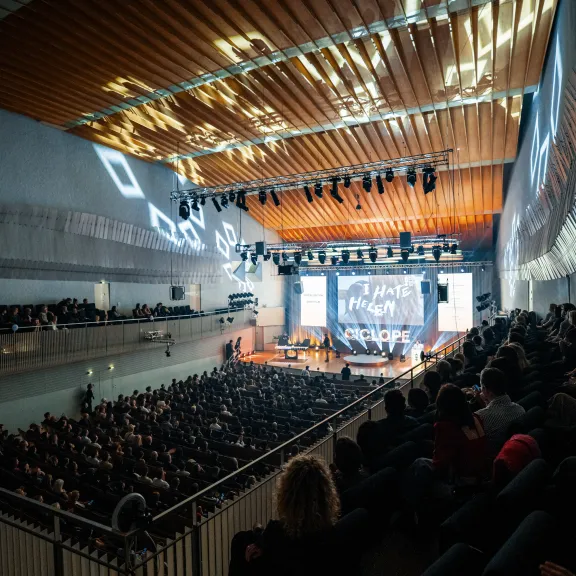 Großer Konzertsaal mit vollbesetztem Publikum und beleuchteter Bühne.