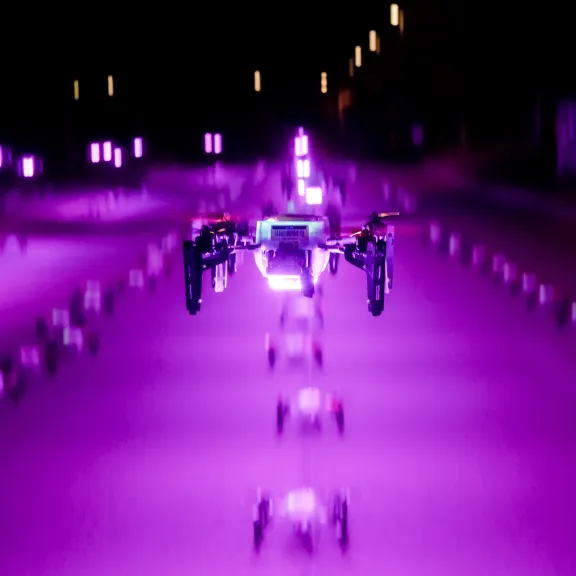 Lila leuchtende Drohne fliegt nachts hoch. Auf dem Boden sind weitere Drohnen aufgereiht.