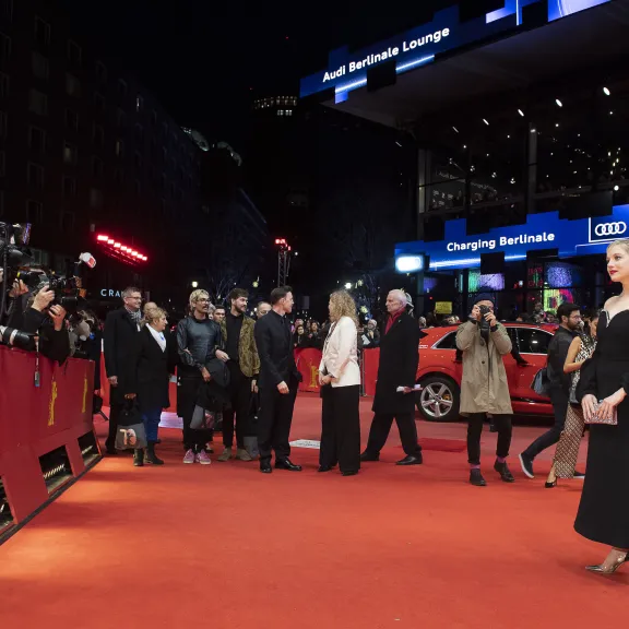 Frau in schwarzem Kleid posiert auf dem roten Teppich vor Fotografen und Publikum bei Nacht.