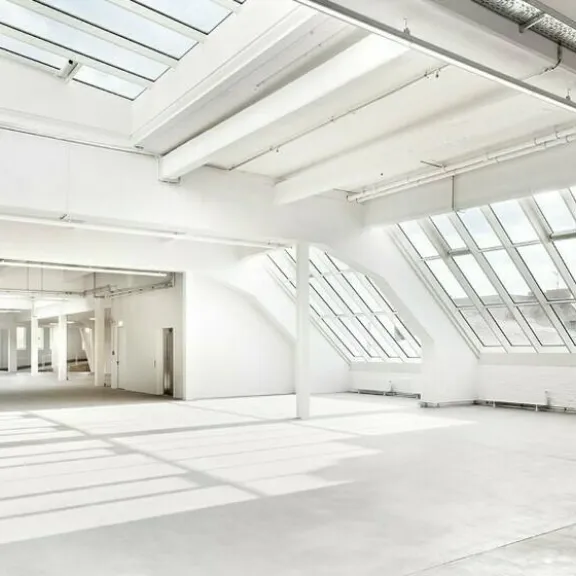 Helle, leere Industriehalle mit großen Fenstern und Oberlichtern.