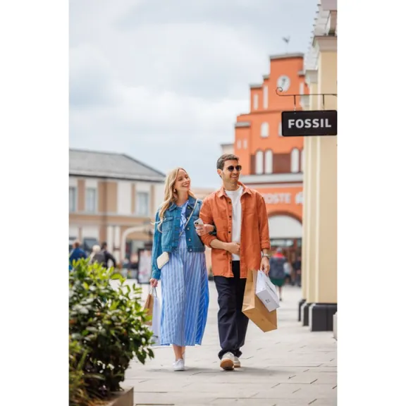 Junges Paar spaziert lächelnd mit Einkaufstüten durch eine Einkaufsstraße.