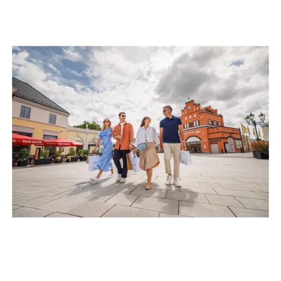 Vier Personen gehen lachend durch eine sonnige Fußgängerzone mit historischen Gebäuden.