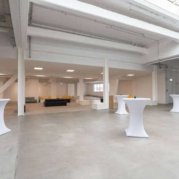 Großer, heller Raum mit Stehtischen und einer Sitzecke im Hintergrund.