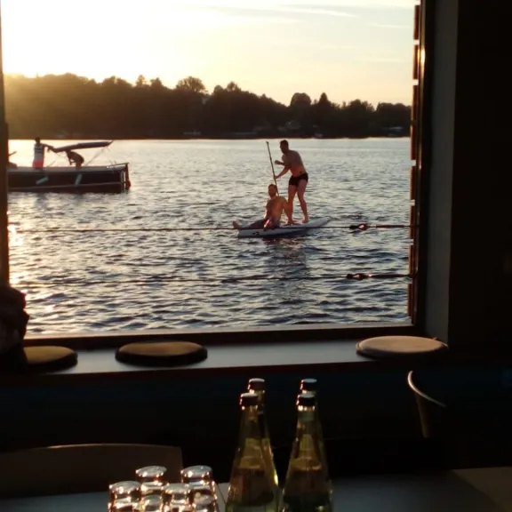 Zwei Menschen beim Stand-Up-Paddling auf einem See bei Sonnenuntergang, Flaschen im Vordergrund.