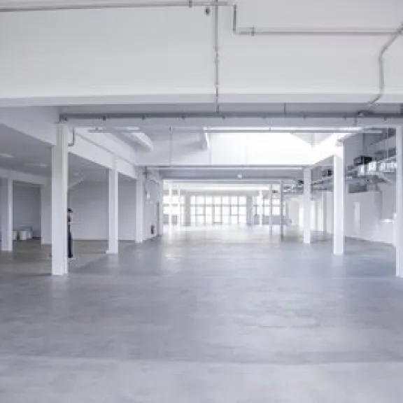 Leere, helle Lagerhalle mit weißen Wänden und Betonboden