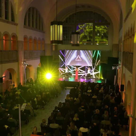 Bunt beleuchtete Bühne vor großem Publikum in einer festlichen Halle