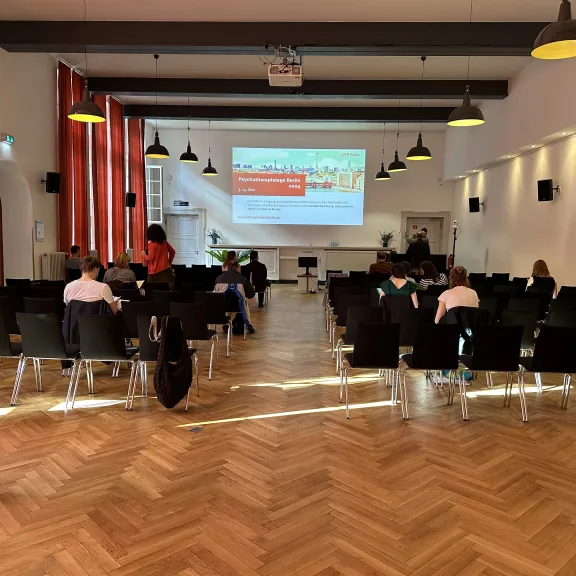 Seminarraum mit Stuhlreihen, Teilnehmern und Präsentation auf Leinwand