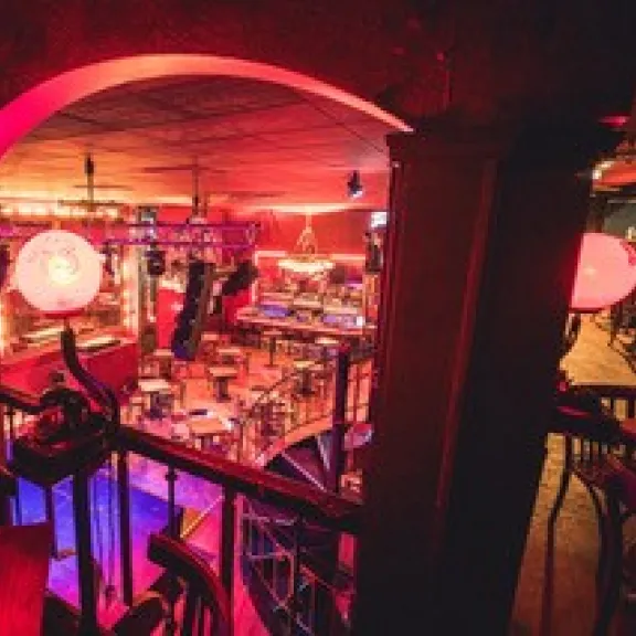 Bar mit rötlicher Beleuchtung, leeren Tischen und festlicher Atmosphäre.