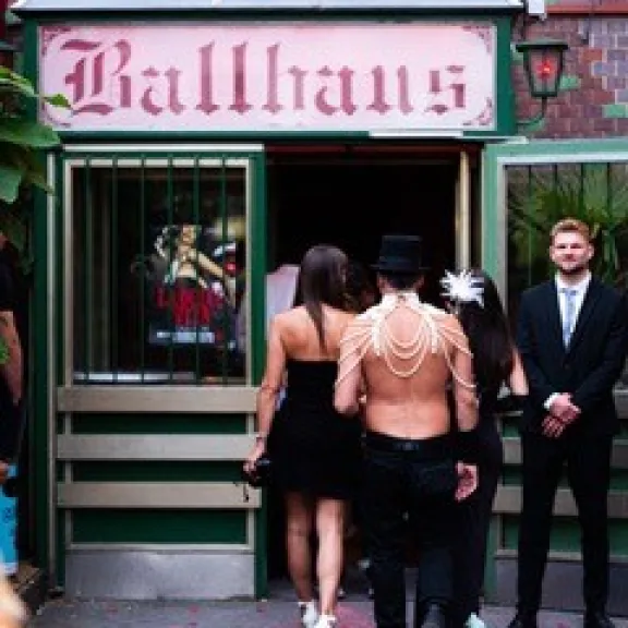 Menschen in Abendkleidung betreten einen Club mit dem Schild "Ballhaus".
