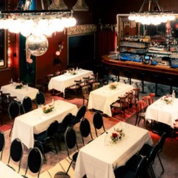 Restaurant mit festlich gedeckten Tischen, schwarzer Bestuhlung und warmer Beleuchtung.