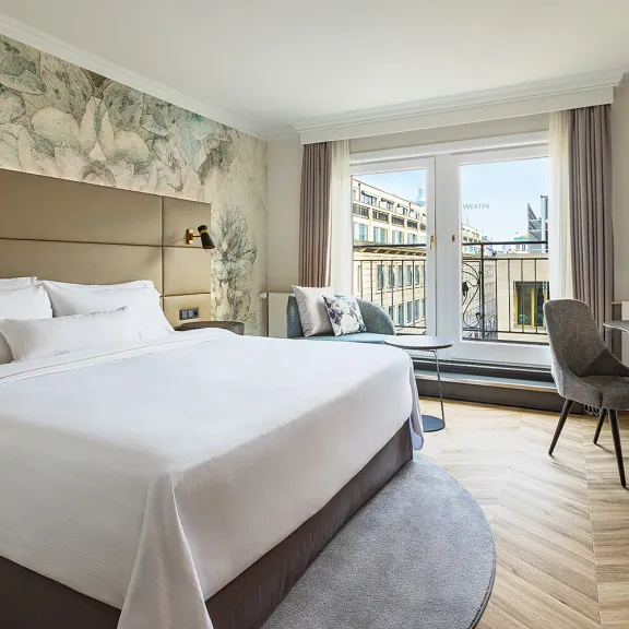 Modernes Hotelzimmer mit großem Bett, Schreibtisch und Balkon mit Stadtblick.