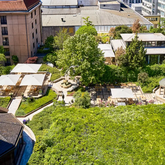 Grüner Innenhof mit Terrassen, Sonnenschirmen und Gartenmöbeln zwischen Gebäuden