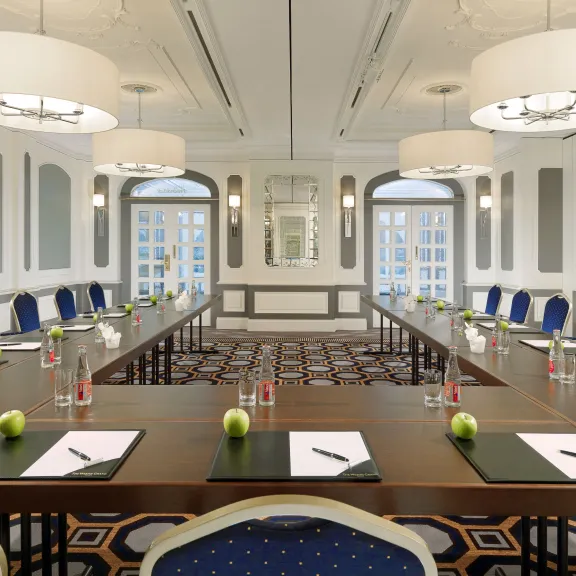 Eleganter Konferenzraum mit U-förmigem Tisch, blauen Stühlen, Wasserflaschen und Äpfeln.