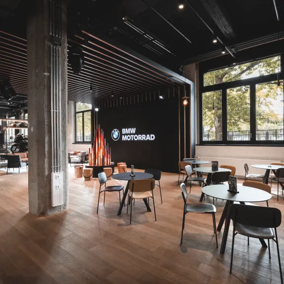 Modernes Café mit Holzboden, runden Tischen und großen Fenstern, viel Tageslicht.