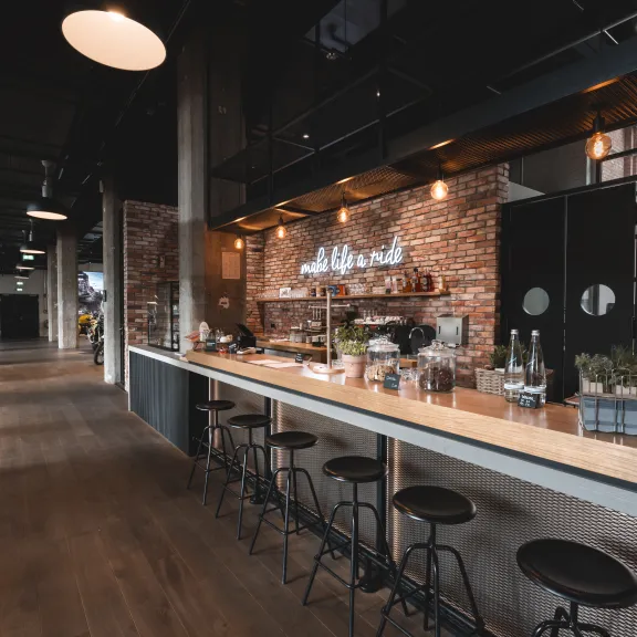 Moderne Café-Bar mit Ziegelwand, langen Tresen und schwarzen Hockern in industrialem Stil.