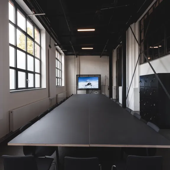 Großer, leerer Konferenzraum mit langem Tisch und Bildschirm am Ende.