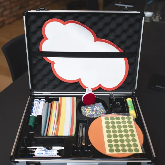 Offener Moderationskoffer mit Stiften, Karten und Moderationsmaterialien auf einem Tisch.