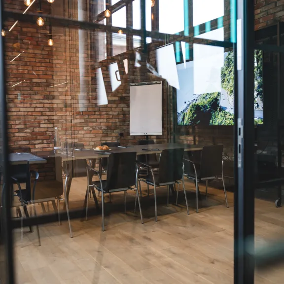 Moderner Besprechungsraum mit Holzboden, Backsteinwand, Glastür und Flipchart.