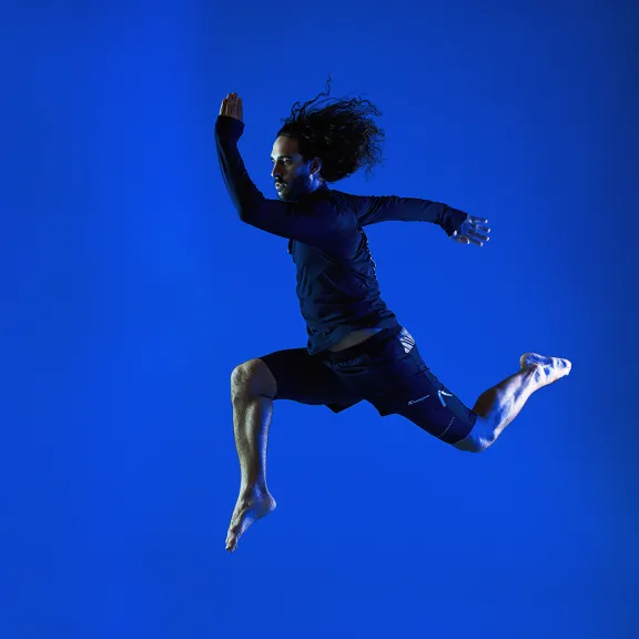 Person springt in der Luft vor blauem Hintergrund.