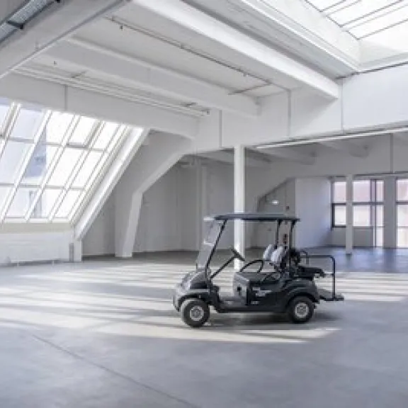Ein Golfwagen steht in einer großen, lichtdurchfluteten Industriehalle.