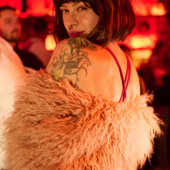 Frau mit dunklen Haaren, Tattoo und Felljacke, rotes Licht im Hintergrund