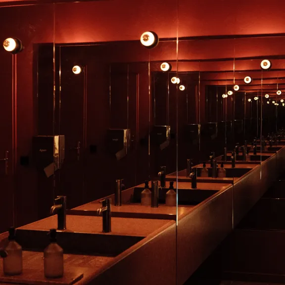 Sanitärbereich von CLINKER mit Spiegelwänden und roten Akzenten.
