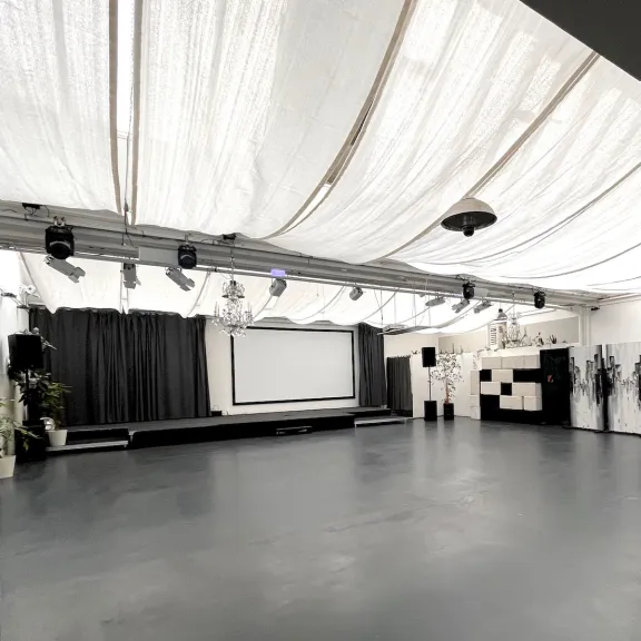 Helle leere Eventfläche in der Forum Factory Berlin mit Bühne, Vorhang und Projektionsleinwand.