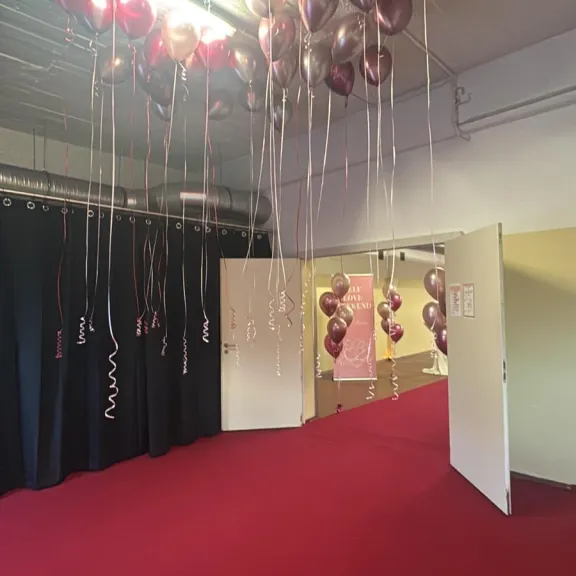 Viele rosa und goldene Ballons schweben an der Decke über einem roten Teppich.