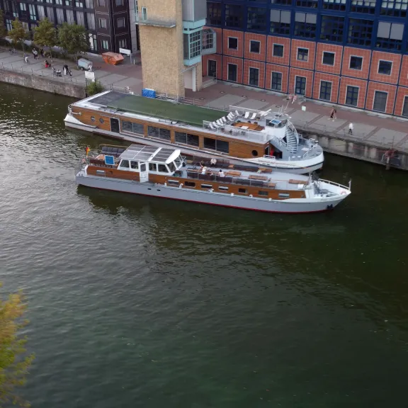 Zwei Ausflugsschiffe liegen nebeneinander an einem Kai vor Backsteingebäuden.