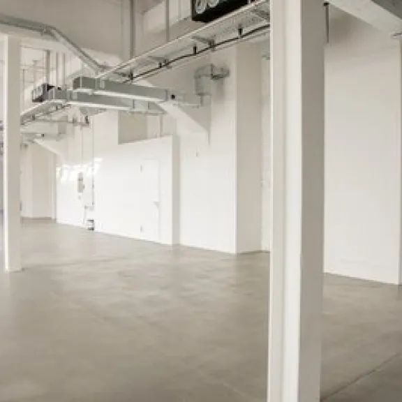 Helle, leere Industriehalle mit weißen Wänden und großen Fenstern
