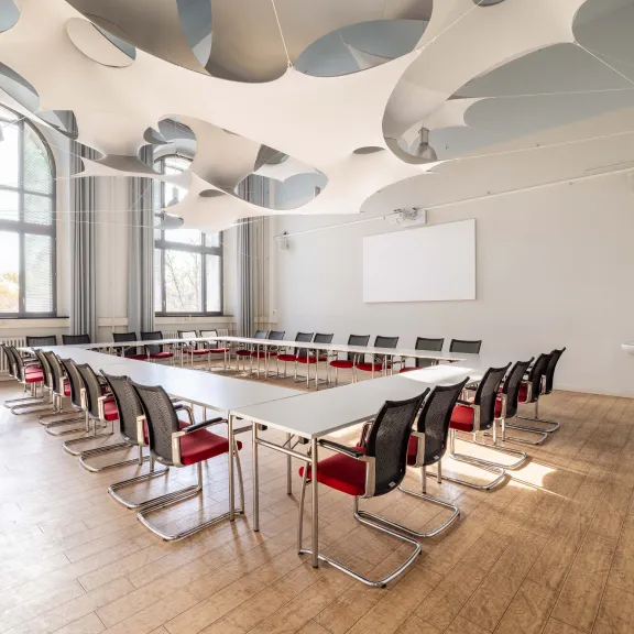 Heller Konferenzraum mit U-förmigen Tischen und modernen Stühlen.