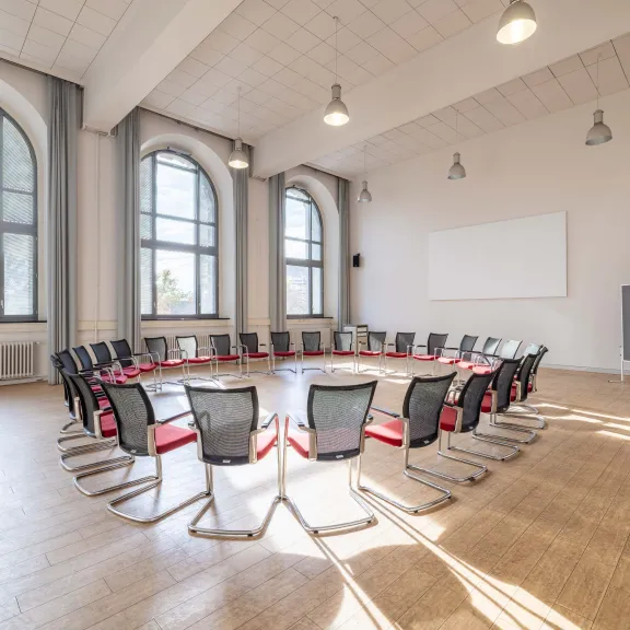 Heller Seminarraum mit Stuhlkreis, großen Fenstern und Holzboden.