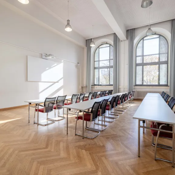 Heller, leerer Seminarraum mit großen Fenstern und modernen Tischen und Stühlen.