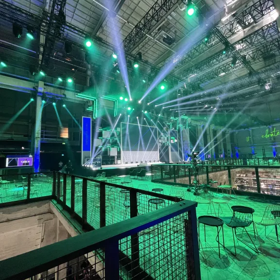 Große Veranstaltungshalle mit grüner Beleuchtung, leeren Stühlen und Bühne