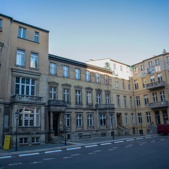 Mehrstöckiges gelbes Wohnhaus mit geparktem roten Transporter vorne.