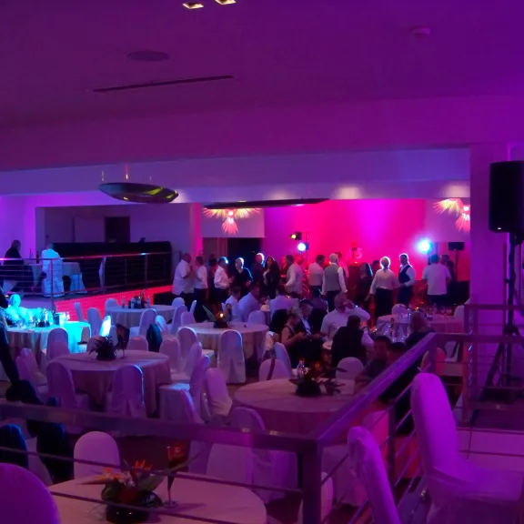 Viele Menschen sitzen an Tischen in lilanem Licht in einem großen Raum