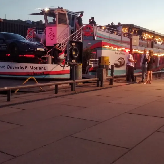 Beleuchtetes Ausflugsschiff am Steg, Auto steht auf dem Deck, Menschen stehen am Ufer.
