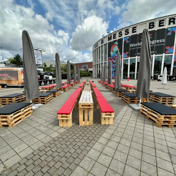 Holzbänke mit roten Polstern und grauen Sonnenschirmen vor der Messe Berlin.