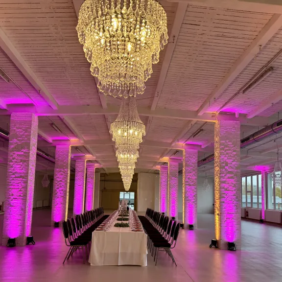 Langer Tisch in elegantem Saal mit Kronleuchtern und lila beleuchteten Säulen.