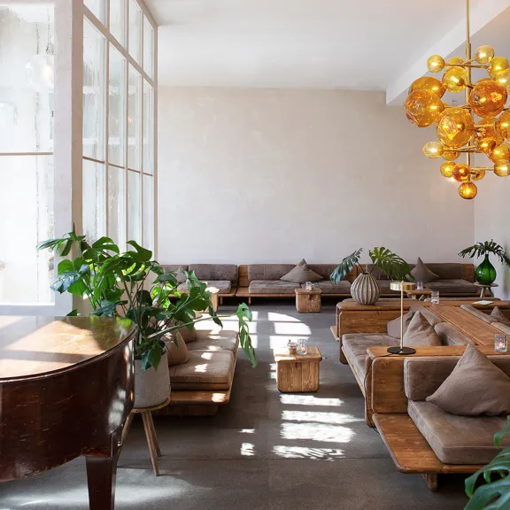 Die lichtdurchflutete Lobby vom Michelberger Hotel mit Ledersofas, Pflanzen und Piano