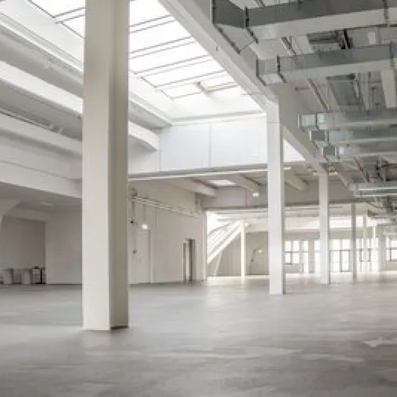 Große, helle Halle mit weißen Wänden und Fenstern im Dach, industrieller Stil.